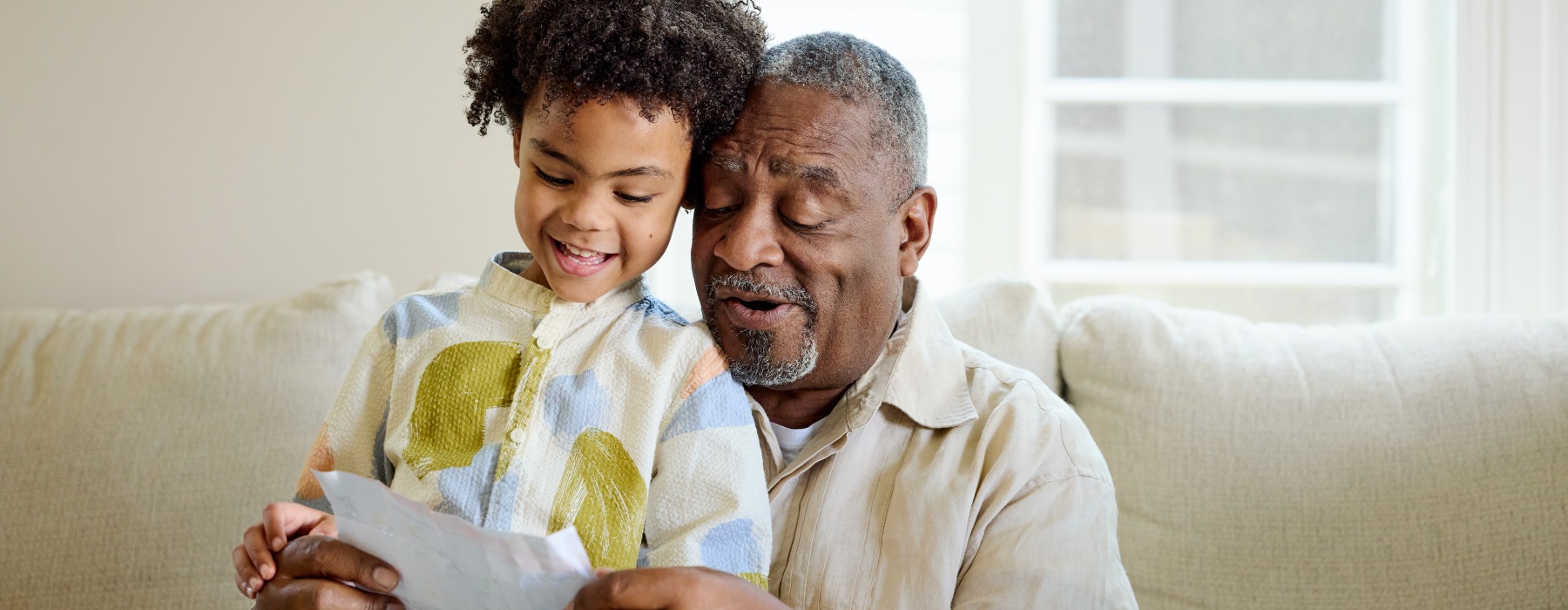 Grandfather and grandson sharing a special moment together while looking at a piece of paper on the couch.