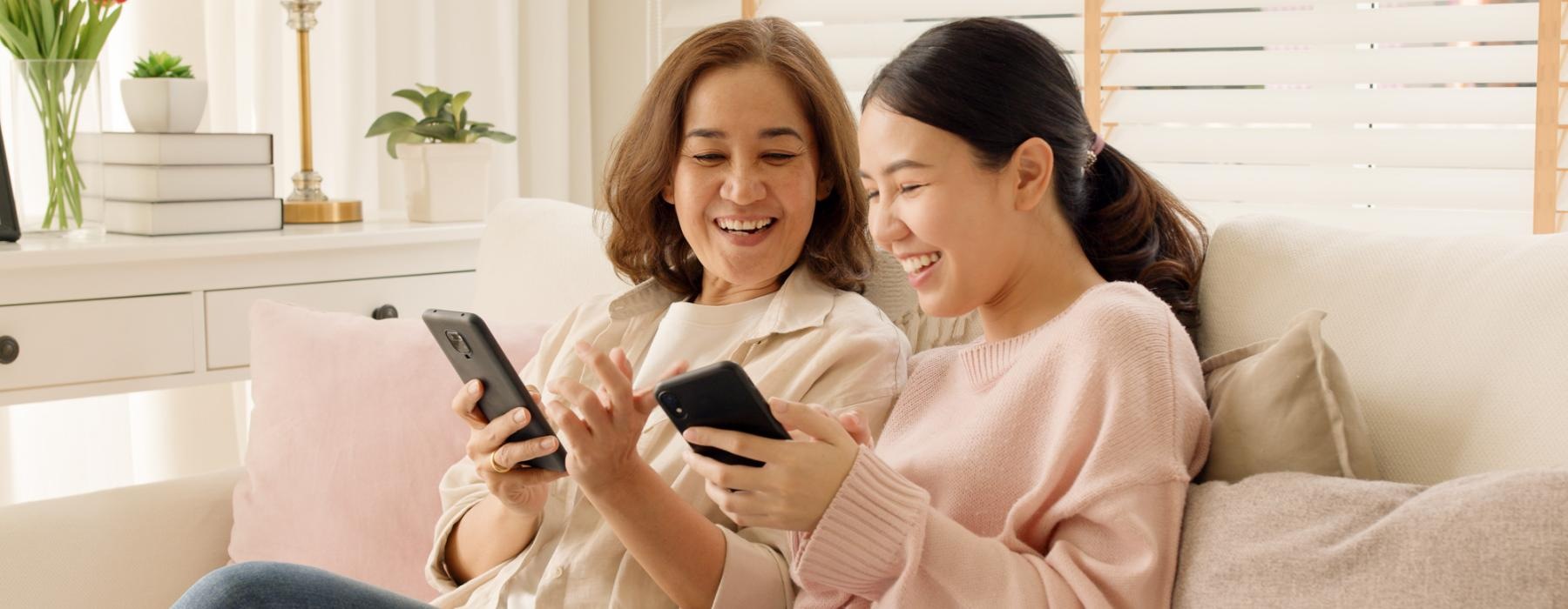 a couple of women sitting on a couch looking at a tablet